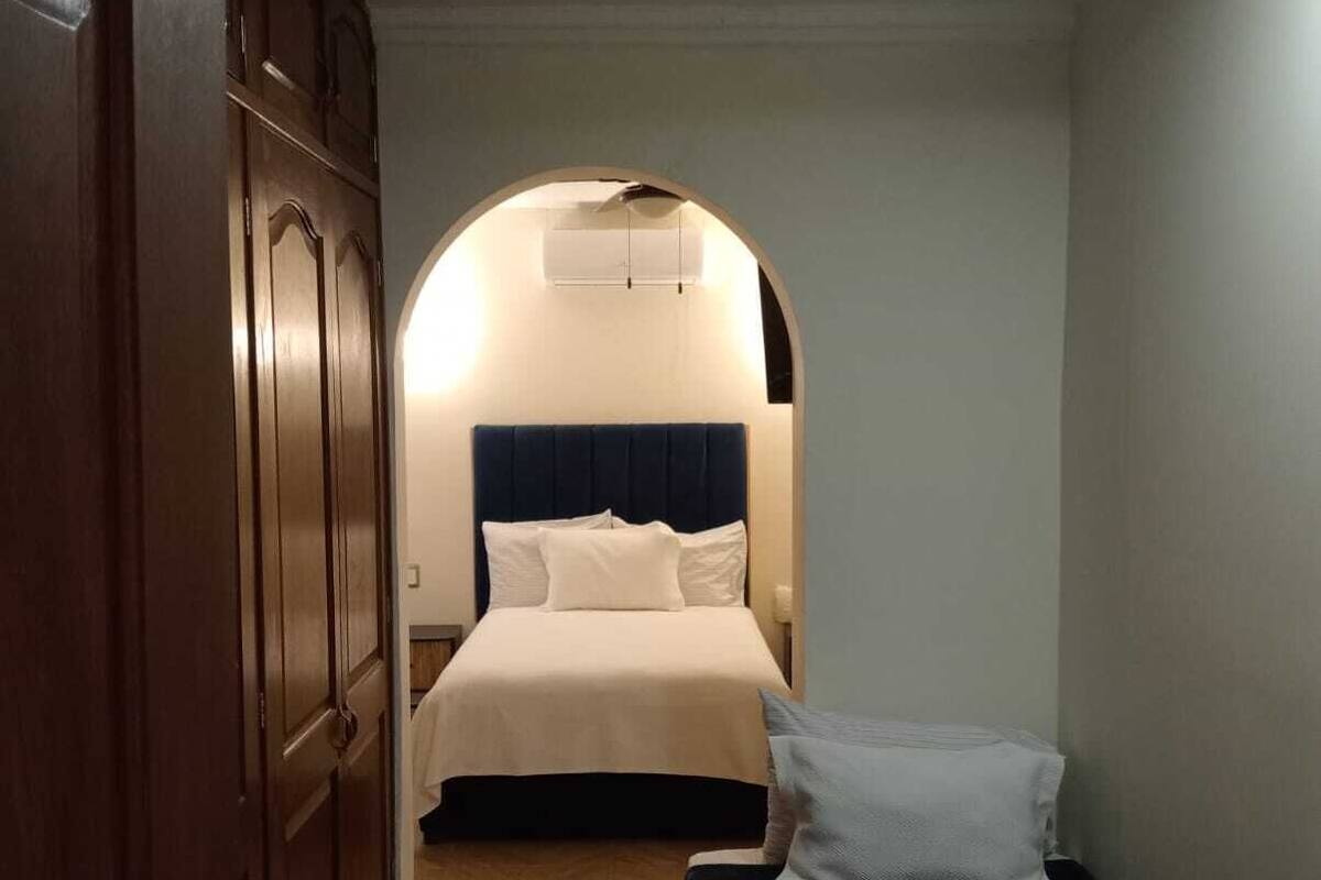 Un pasillo estrecho que da a un dormitorio con cama, un banco y un armario.