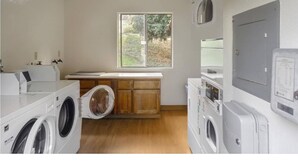 A laundry room with multiple washing machines, a wooden bench, and a window providing natural light.