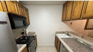 A compact kitchen with wooden cabinets, a stainless steel refrigerator, a microwave, an oven, a dishwasher, and a granite countertop.