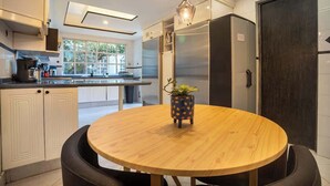 A modern kitchen with a round wooden table, a potted plant, and a large refrigerator.