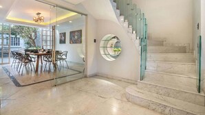Un intérieur moderne avec un escalier en verre, un coin repas avec des chaises et une étagère circulaire en verre.