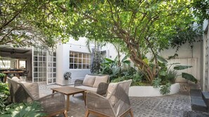 An outdoor patio with wicker furniture, a large tree, and a view of a building with large windows.