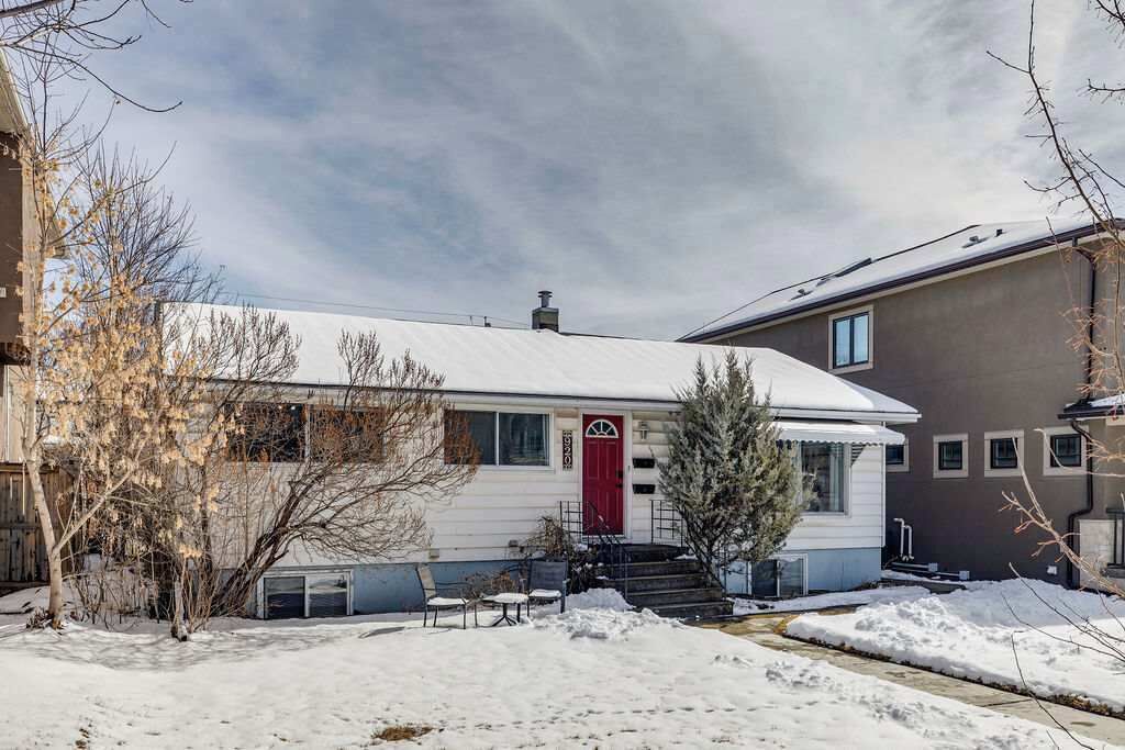 A single-story house with a red door, a small porch with chairs, and a snow-covered yard.