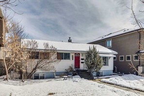 A single-story house with a red door, a small porch with chairs, and a snow-covered yard. - 80 min Banff, Minutes from Foothills Hospital (Calgary)