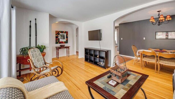 Uma sala de estar com sofá, mesa de centro, televisão, área de jantar com cadeiras e estante de livros.