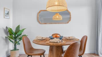 A dining area with a round wooden table, brown leather chairs, a woven pendant light, a mirror, and a potted plant.