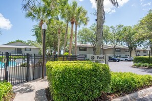 A gated pool area with a sign indicating pool hours, surrounded by lush greenery and tall palm trees. - 2BR Family Retreat - River Views, Pool & Tennis, Sleeps 6 (St. Augustine)