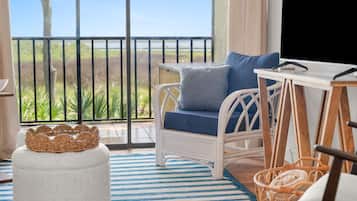A balcony with wicker furniture, a striped rug, and a view of greenery.