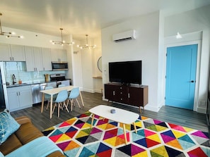 A modern living room with a sofa, a dining table, a TV, and a colorful rug. - Penthouse Suite, Top Floor Panoramic Ocean View with AC & Free Parking (Honolulu)
