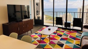 Un balcón con vista al mar, un televisor de pantalla plana, un comedor y una alfombra colorida.