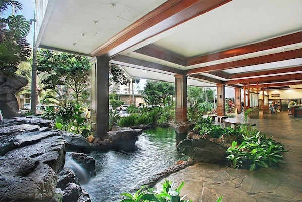 A hotel lobby with a water feature, stone seating, and indoor plants. - Penthouse Suite, Top Floor Panoramic Ocean View with AC & Free Parking (Honolulu)