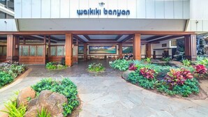 Entrada de un hotel con un letrero que dice 'wakiki banyan', un área de acceso cubierta y jardines ajardinados con rocas y plantas.