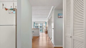 Um corredor com um refrigerador, uma porta com venezianas e vista para um quarto com varanda.