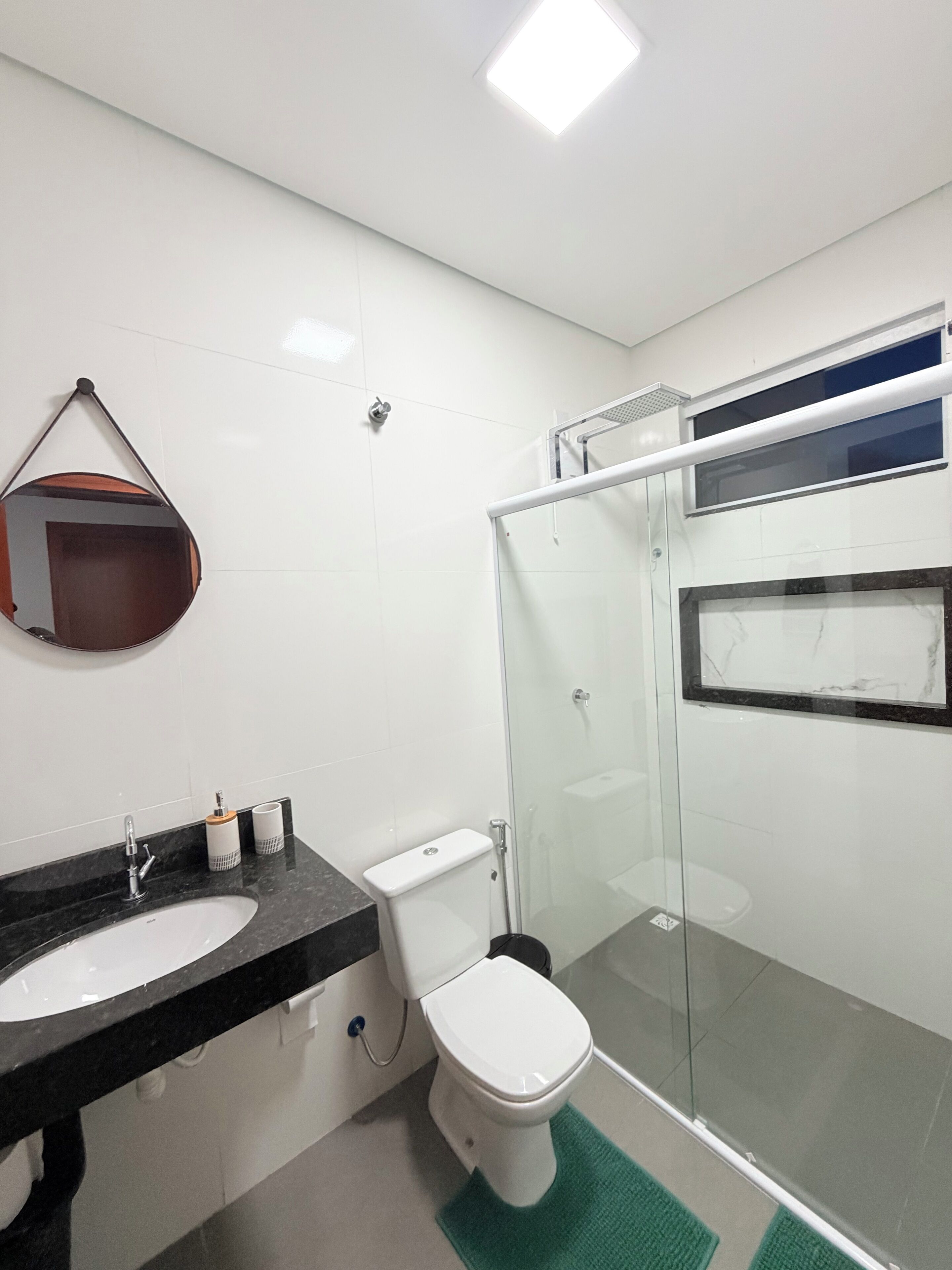 Une salle de bain moderne avec une douche à parois de verre, des toilettes blanches et un lavabo sur un plan de toilette noir.