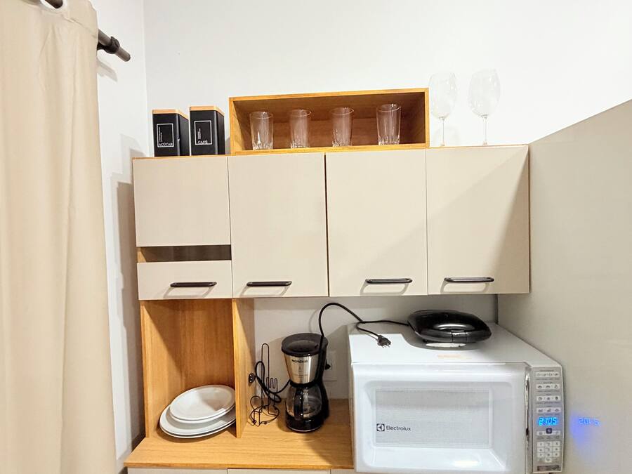 A compact kitchenette with a microwave, coffee maker, and storage cabinets.