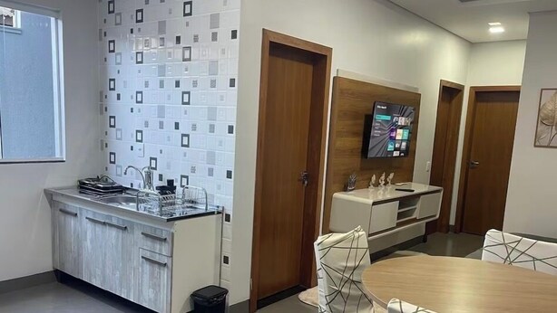 A modern kitchen with a built-in stove, a sink, and a small trash bin. There is a dining area with a round table and chairs. - Edifício VIvaVida (Sinop)