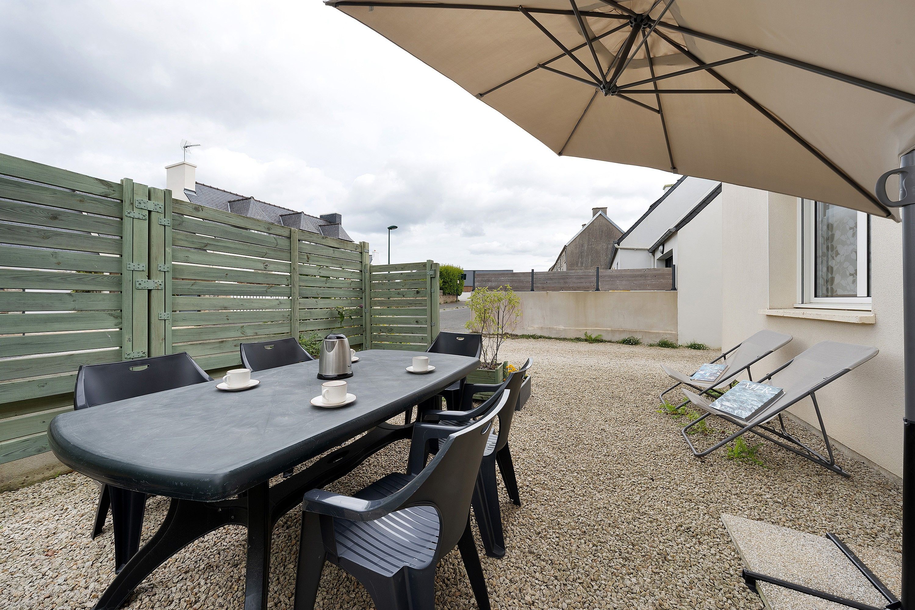 An outdoor patio with a table and chairs, a large umbrella, and a gravel ground.