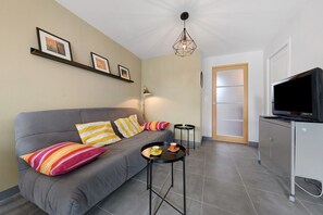 A modern living room with a grey sofa, colorful pillows, a black coffee table, a floor lamp, a flat-screen TV, and a door with frosted glass panels. - Location 300 m from the Beach (Roscoff)
