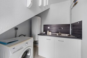 A compact kitchen with a built-in washing machine, a sink, and a mirror above it. - Location 300 m from the Beach (Roscoff)