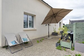 Eine Terrasse mit zwei Liegestühlen, einem Tisch und einem Sonnenschirm.