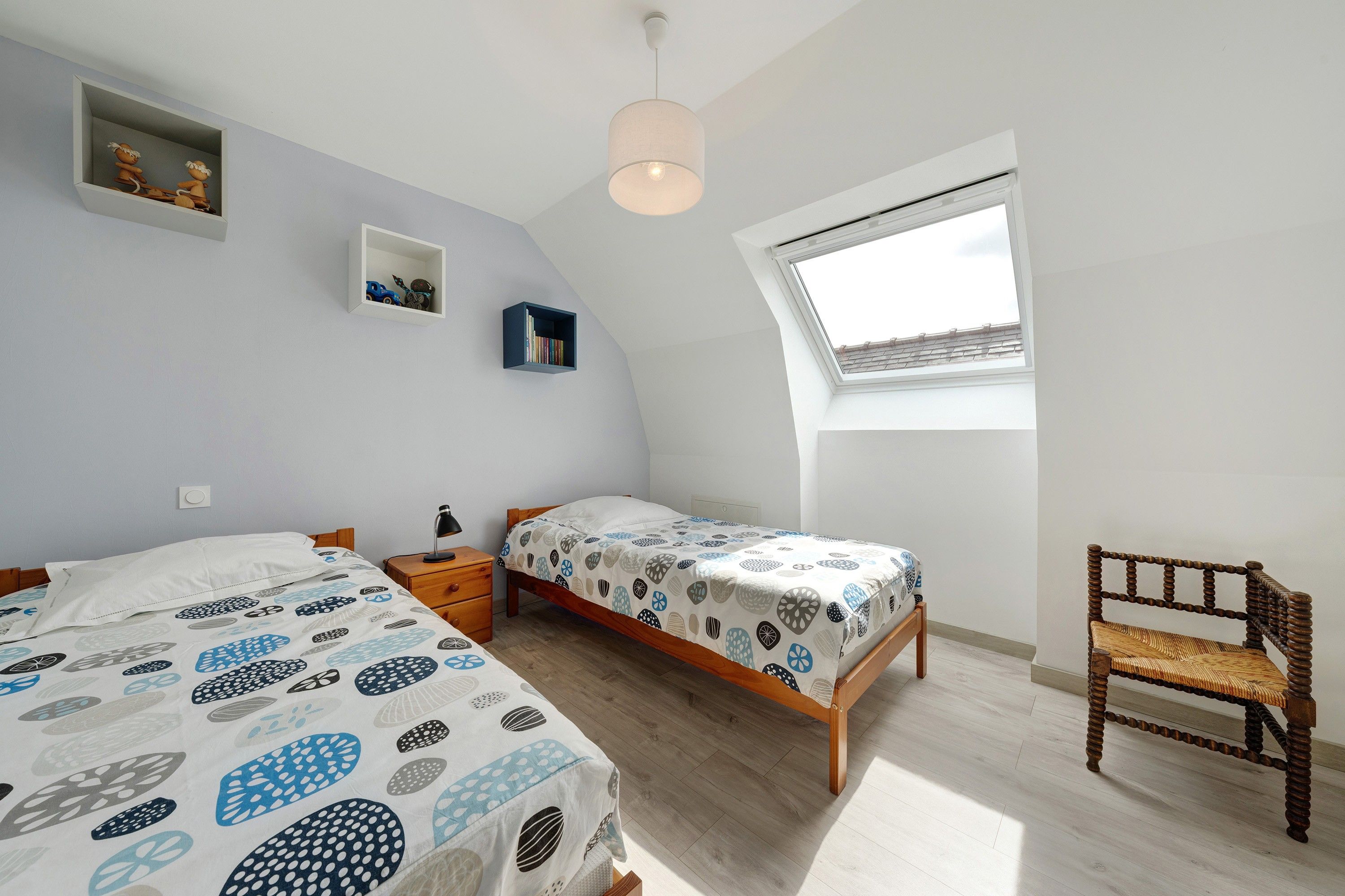 Camera da letto con due letti, una finestra, una sedia e una lampada a soffitto.