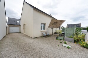 A residential property with a gravel driveway, a white garage, a beige house, a window, a door, and a large umbrella. - Location 300 m from the Beach (Roscoff)