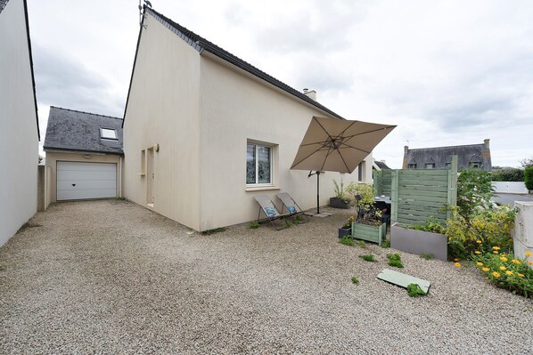 Een woonhuis met een grindpad, een witte garage, een beige huis, een raam en een deur, en een grote parasol.