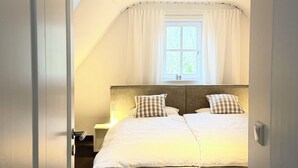 Ein Schlafzimmer mit einem großen Bett, einem Fenster mit Vorhängen, einer Deckenleuchte und einer Tür.