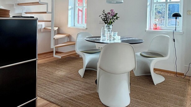Ein modernes Interieur mit einer Treppe, einem Essbereich mit rundem Tisch und Stühlen sowie einem großen Fenster.