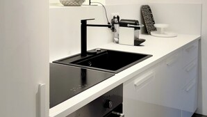 Eine moderne Küche mit weißen Schränken, einer schwarzen Induktionskochplatte, einem eingebauten Backofen, einem Fenster mit Aussicht und einer schwarzen Stehlampe.