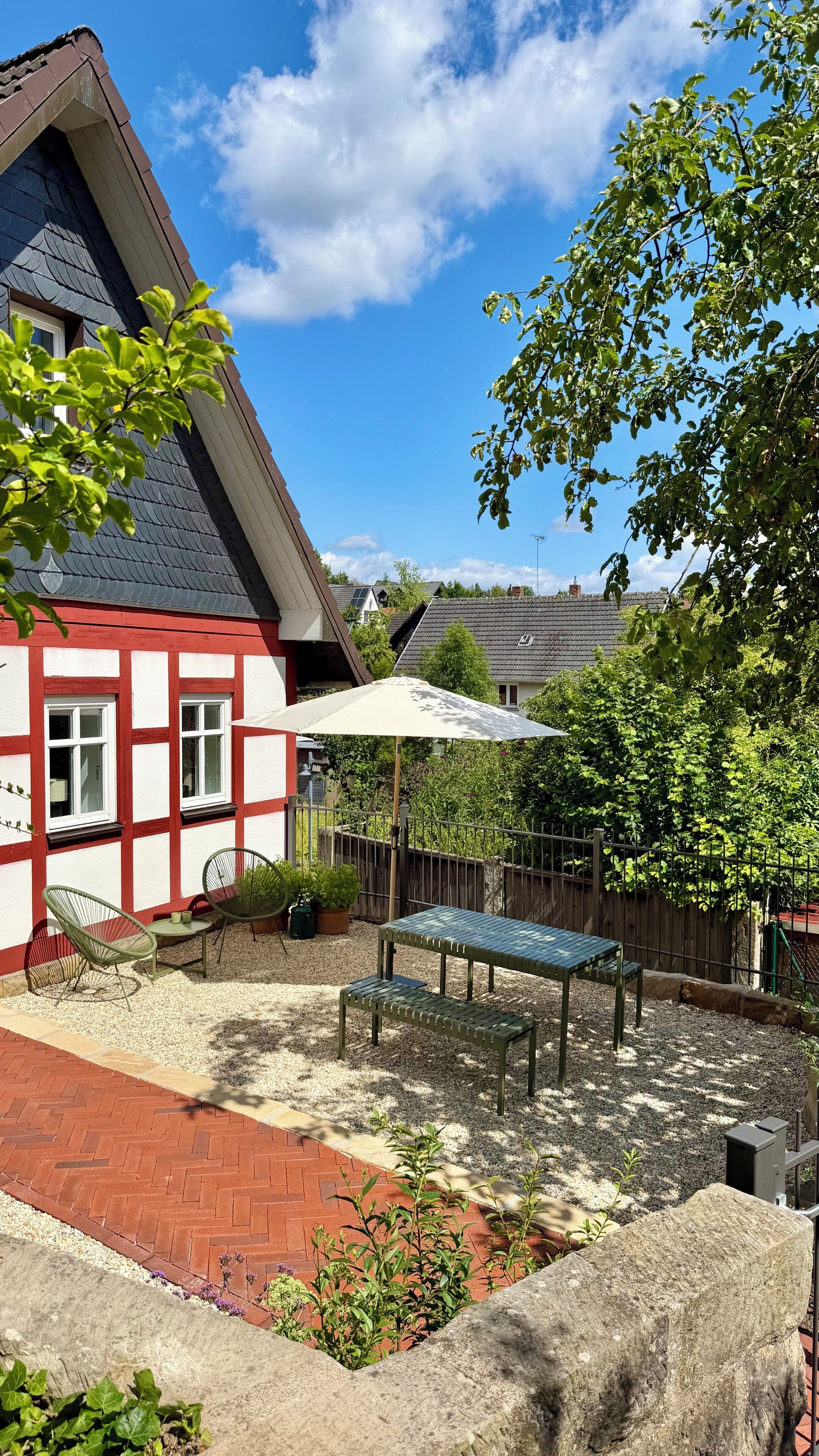 A courtyard with a patio table and chairs, a white umbrella, and a red brick pathway.