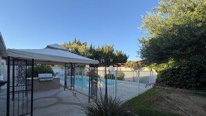 Un patio trasero con piscina, un porche cubierto y un área cercada.