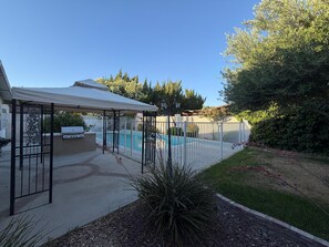 Ein Garten mit Pool, überdachter Terrasse und umzäunter Fläche.