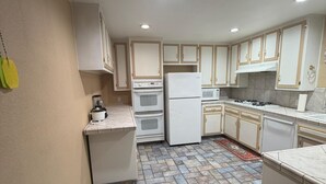 Una cocina compacta con electrodomésticos blancos, paredes color beige y piso estampado.