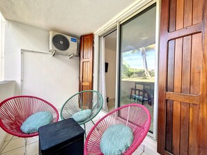 Een kamer met een schuifglazen deur, een houten deur en een plafondventilator. Er staan vier rieten stoelen met kussens.