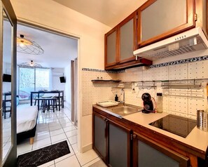 A kitchen with wooden cabinets, a sink, and a stove. There is a dining area with a table and chairs visible through an open door.