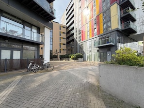 A modern urban building with a brick-paved entrance, a bicycle parked outside, and a gated area with greenery. - Bright 3BDR Canalside Flat in Hackney (London)