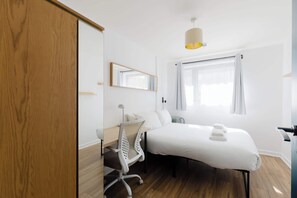 Ein Hotelzimmer mit Bett, Schreibtisch, Stuhl, Spiegel, Fenster und Deckenleuchte.