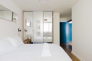 Ein Hotelzimmer mit einem großen Bett, einem Holfnachtkästchen, einem Spiegel und einer Schiebetür zum Badezimmer.