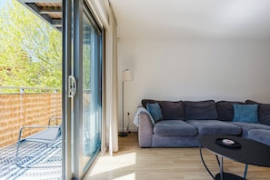 A modern living room with a grey sofa, a small round table, and a glass door leading to an outdoor area with a wooden fence. - Bright 3BDR Canalside Flat in Hackney (London)