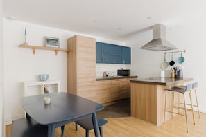 A modern kitchen with wooden cabinets, a built-in microwave, and a bar area with stools. - Bright 3BDR Canalside Flat in Hackney (London)