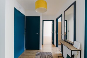 Ein Flur mit einer blauen Tür, einer gelben Pendelleuchte, einem Holzkonsolentisch mit einem Gerät und einem Spiegel.