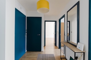 Ein Flur mit einer blauen Tür, einer gelben Pendelleuchte, einem Holzkonsolentisch mit einem Gerät und einem Spiegel.