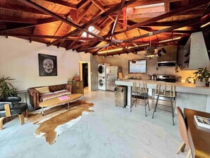 A spacious living area with a high ceiling, a sofa, a coffee table, a rug, a washing machine, a refrigerator, a bar area with stools, and a kitchen with a stove and oven. - Welcoming 1-bedroom house with AC / pool / table tennis in vibrant Los Angeles (Los Angeles)