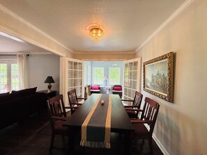 Ein Esszimmer mit einem langen Tisch, Stühlen, einer Kandelaber und einem gerahmten Bild an der Wand.
