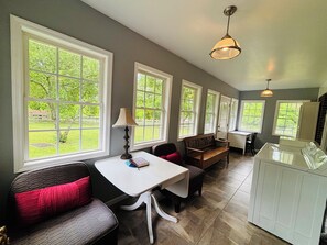 A spacious kitchen with large windows, a dining area with a bench, and a white table.