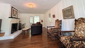 Ein Zimmer mit Kamin, Holzboden, einem gemusterten Sessel und einem an der Wand befestigten Schild.