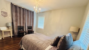Ein Schlafzimmer mit einem Bett, zwei Stühlen, einem Schreibtisch, einer Chandelier und einem Fenster mit Jalousien.