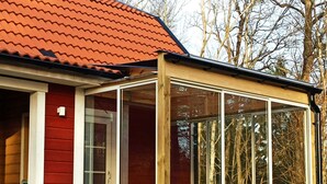 Una casa de madera con techo rojo y un cerramiento de vidrio.