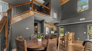 Ein geräumiger Essbereich mit Holztisch und -stühlen, eine Treppe mit hölzernen Geländern sowie ein Küchenbereich mit Schränken und Geräten.
